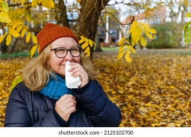 秋公園でティッシュペーパーで鼻をかむ年配の女性の写真素材