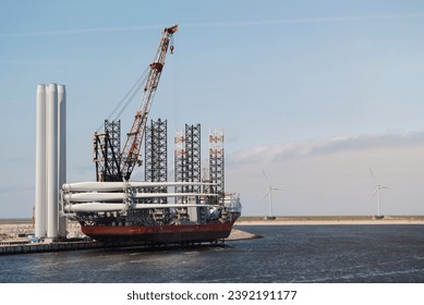 Self Elevating Wind Installation Vessel In The European Port During Process Of Heavy Lift Operation And Loading Of The Wind Blades On Deck. Offshore Support Construction DP Vessel Alongside Stock fotografie