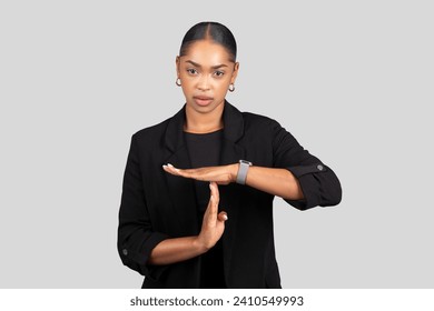 Serious African American businesswoman shows a timeout hand signal, calling for a break or pause in action, with a focused expression against a plain background, studio Arkistovalokuva