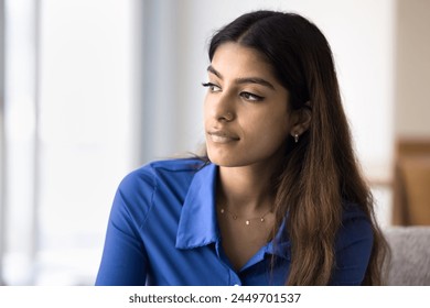 Serious pensive beautiful Indian woman looking away with focus on deep thoughts, sitting on home couch, thinking on problems, troubles. Thoughtful silent young adult girl making decision Stock-foto