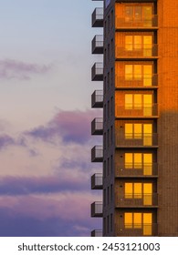 The setting sun casts a warm glow on the brick facade of a residential high-rise in Gothenburg, Sweden. Balconies line one side, offering a view of the pink and blue hues of the evening sky. Foto Stock