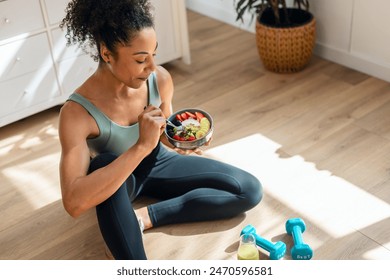 自宅のキッチンで床に座って健康的なフルーツボウルを食べる運動女性のショットの写真素材