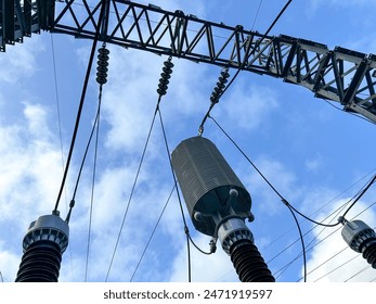 Shot of Capacitive Voltage Transformes with the middle one having a wave trap device on top under steel gantry tower with insulators and conductors heading to transmission tower Stockfoto