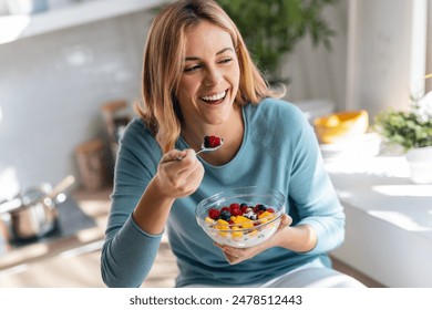 Shot of kind beautiful woman eating a healthy fruit bowl while sitting on the table in the kitchen at home Stock-foto