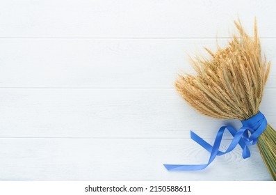 Shavuot jewish holiday celebration. Bouquet of golden ripe wheat with a blue ribbon. White wood board table with field of wheat. Background for Shavuot celebration. Top view. Mock up. Stock-foto