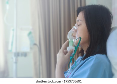 Sick beautiful female in blue cloth hold nasal mask with respiratory problem in hospital room. Asian woman patient inhalation therapy by the mask of inhaler with soft stream smoke from bronchodilator. स्टॉक फ़ोटो