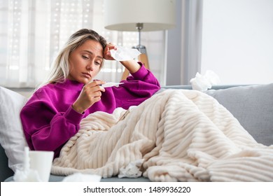 Sickness, seasonal virus problem concept. Woman being sick having flu lying on sofa looking at temperature on thermometer. Sick woman lying in bed with high fever. Cold flu and migraine. स्टॉक फ़ोटो