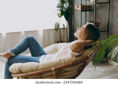 Side profile back view calm blonde young woman wearing casual clothes sit in armchair look camera stay at home hotel flat rest relax spend free spare time in living room indoor. People lounge concept Foto stock