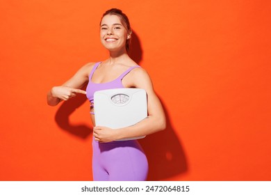 Side view young fitness trainer instructor sporty woman sportsman wear purple top clothes spend time in home gym hold point on scales isolated on plain orange background. Workout sport fit abs concept Stockfoto