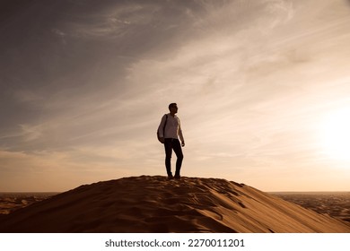 
日没時に砂丘の上に立つバックパックを持つ男性のシルエット。の写真素材