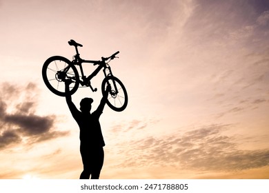 A silhouette of a cyclist lifting their bicycle overhead, celebrating against a beautiful sunset backdrop with a dramatic sky. Foto stock