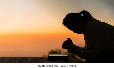 Silhouette of woman kneeling down praying for worship God at sky background. Christians pray to jesus christ for calmness. In morning people got to a quiet place and prayed. Banner with copy space. Foto stock