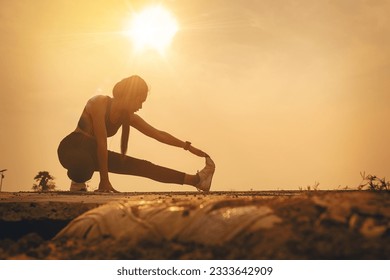 Silhouette of Woman warming up, stretching her muscle at the road track outdoor with sunset background. Fit runner workout and warming up Foto Stock