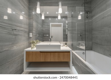 A sleek, modern bathroom featuring a large mirror, elegant lighting, and a stylish sink with wooden accents. The gray marble walls and glass shower enclosure add a touch of luxury. - Φωτογραφία στοκ