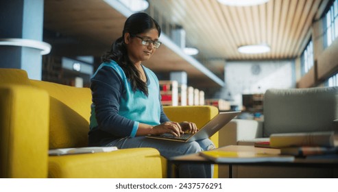 Smart Indian Female Student in Glasses Working on Software Development Assignment in a Quiet Public Library. Young South Asian Woman Using Laptop Computer and Preparing for Examination in College Foto stock