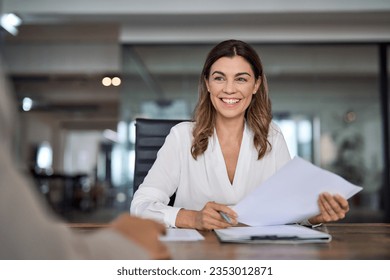 Smiling mature business woman hr holding cv document at job interview. Happy mid aged professional banking manager or lawyer consulting client sitting at workplace in corporate office meeting., fotografie de stoc