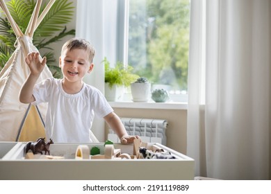 Niño sonriente jugando caja sensorial mesa de arena cinética con materiales de madera de Montessori y animales de granja cerrados. Niños bebés felices disfrutan del desarrollo infantil temprano en la habitación con acampada wigwam Foto de stock