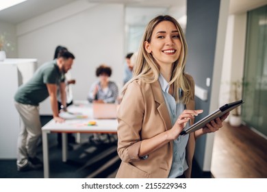 Smiling confident business leader looking at camera and standing in an office at team meeting. Portrait of confident businesswoman with colleagues in boardroom. Using digital tablet during a meeting. Stock-foto