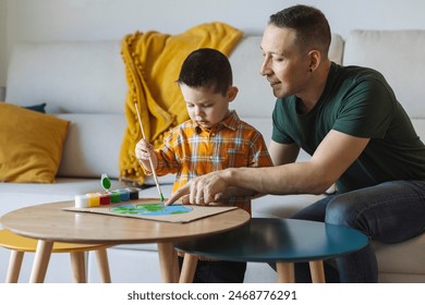 Smiling father teaching son to paint planet earth on cardboard at home: stockfoto