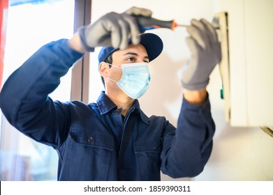 コロナウイルスの大流行によるマスクを着けた温水器を修理する笑顔の技術者の写真素材