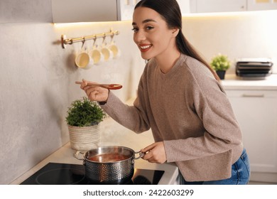 Smiling woman with wooden spoon tasting tomato soup in kitchen – Ảnh có sẵn