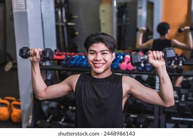 A smiling young man does a set of seated dumbbell shoulder presses. A slim teenager building muscle at the gym. Stock Photo