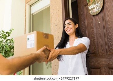 Smiling young woman is receiving a package from a delivery man at the entrance of her home 库存照片