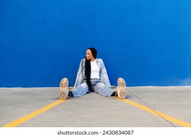Mujer joven sonriente sentada en el suelo frente a la pared azul Foto de stock