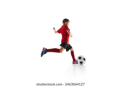 Sporty little boy, kicks ball to make perfect pass in motion against white studio background. Small football player makes goal. Concept of professional sport, championship, youth league, hobby. Ad Foto stock