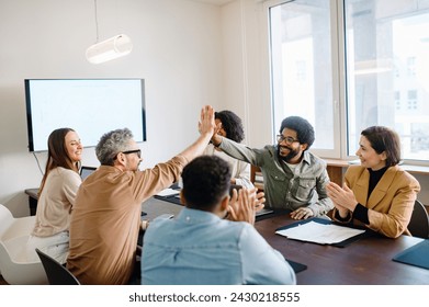 A spirited office team engages in a high-five, highlighting the successful collaboration and energetic atmosphere. Teamwork and the collective success that comes from a well-coordinated effort. 库存照片