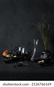 黒い背景に黒いテーブルとコピー用スペースに赤ワイン、ブドウ、イチジク、桑と小枝の2つのガラスの花瓶で静物の写真素材