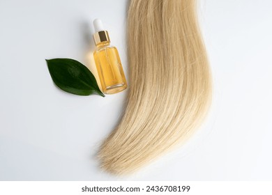 栄養のあるオイルボトルと新鮮な緑の葉を持つ絹のような金髪のストランドは、有機ヘアケアを象徴しています。の写真素材