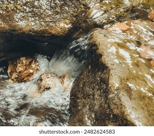 A stream of water flows down a rocky hillside. The water is clear and calm, and the rocks are grey and rough

 Foto Stock