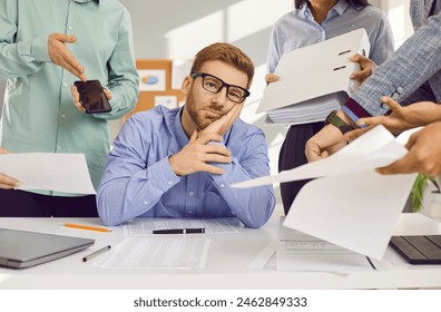 Stress, burnout and tired man sitting at the desk in office frustrated or overwhelmed by coworkers at workplace. Young businessman looking sad at camera. Overworked, multitasking concept. Arkistovalokuva