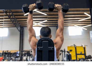 Strong man from behind, training back with dumbbells sitting Stockfoto