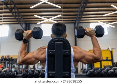 Strong man from behind, training back with dumbbells sitting Stockfoto