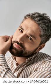 A stylish man with a beard exuding charm in a striped shirt against a neutral studio backdrop., fotografie de stoc