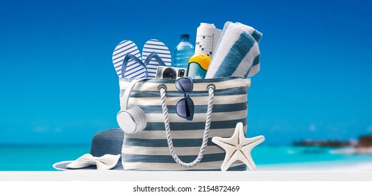 Stylish beach bag with accessories and tropical beach in the background, summer vacations concept Stock Photo
