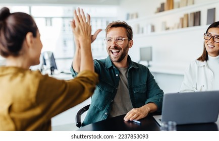 Successful business people giving each other a high five in a meeting. Two young business professionals celebrating teamwork in an office. ஸ்டாக் ஃபோட்டோ
