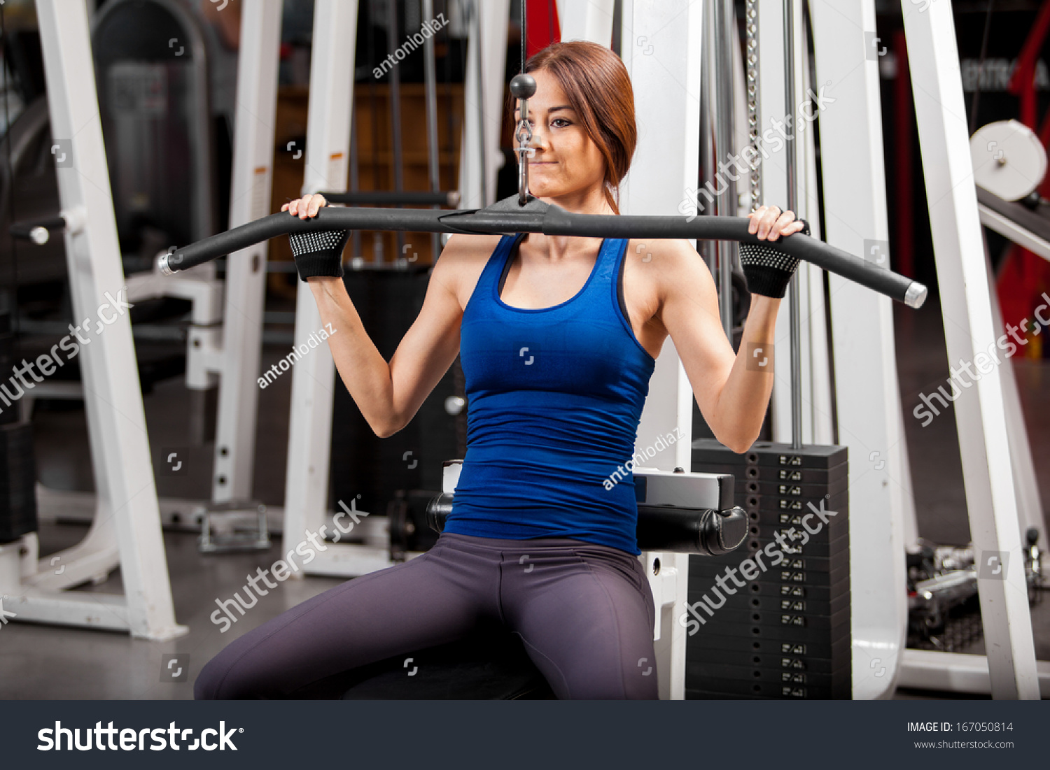 Pretty young athletic woman building some muscle in a simulator at the gym