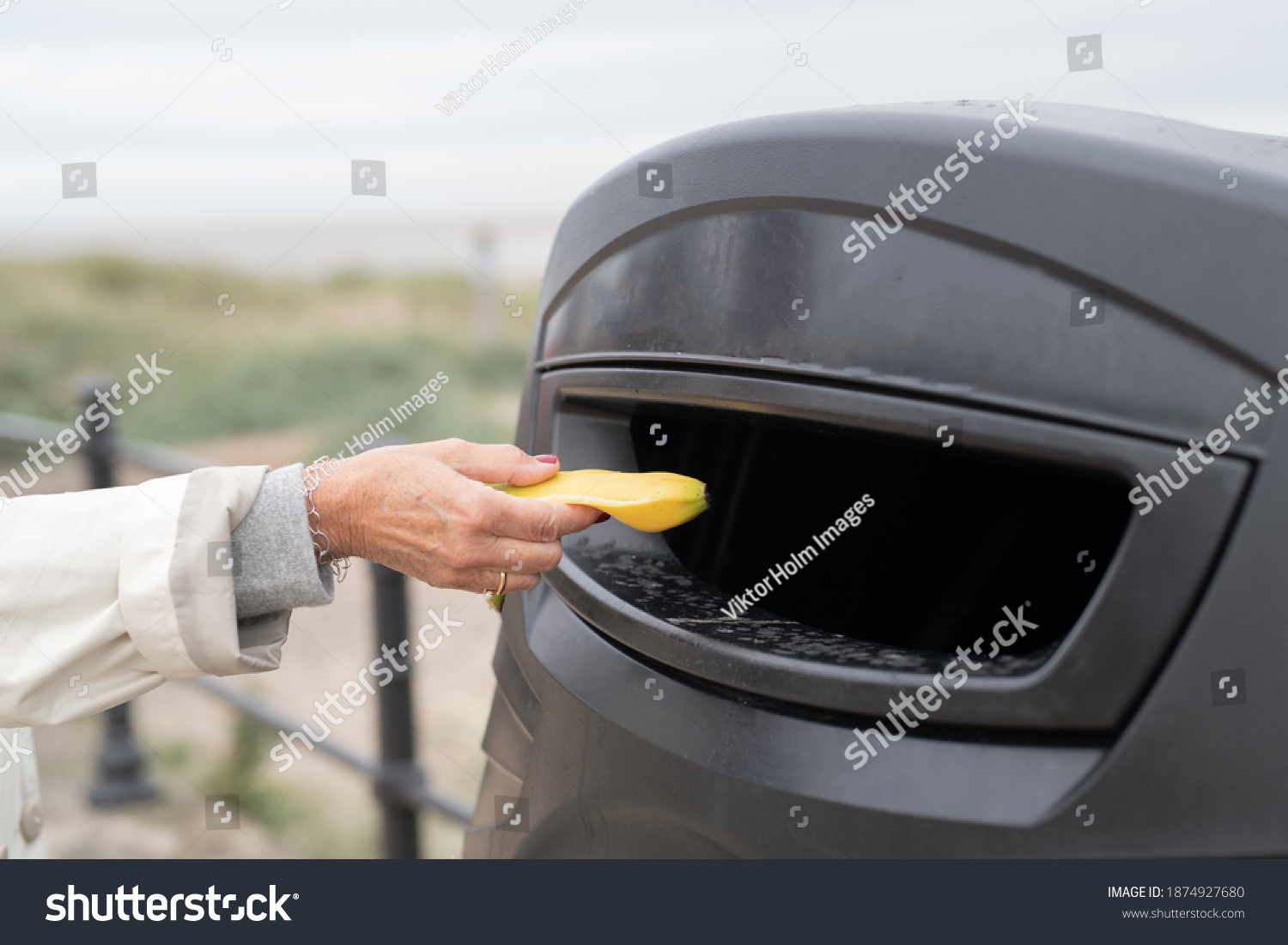 Person putting a banana peel in public outdoor trash can
