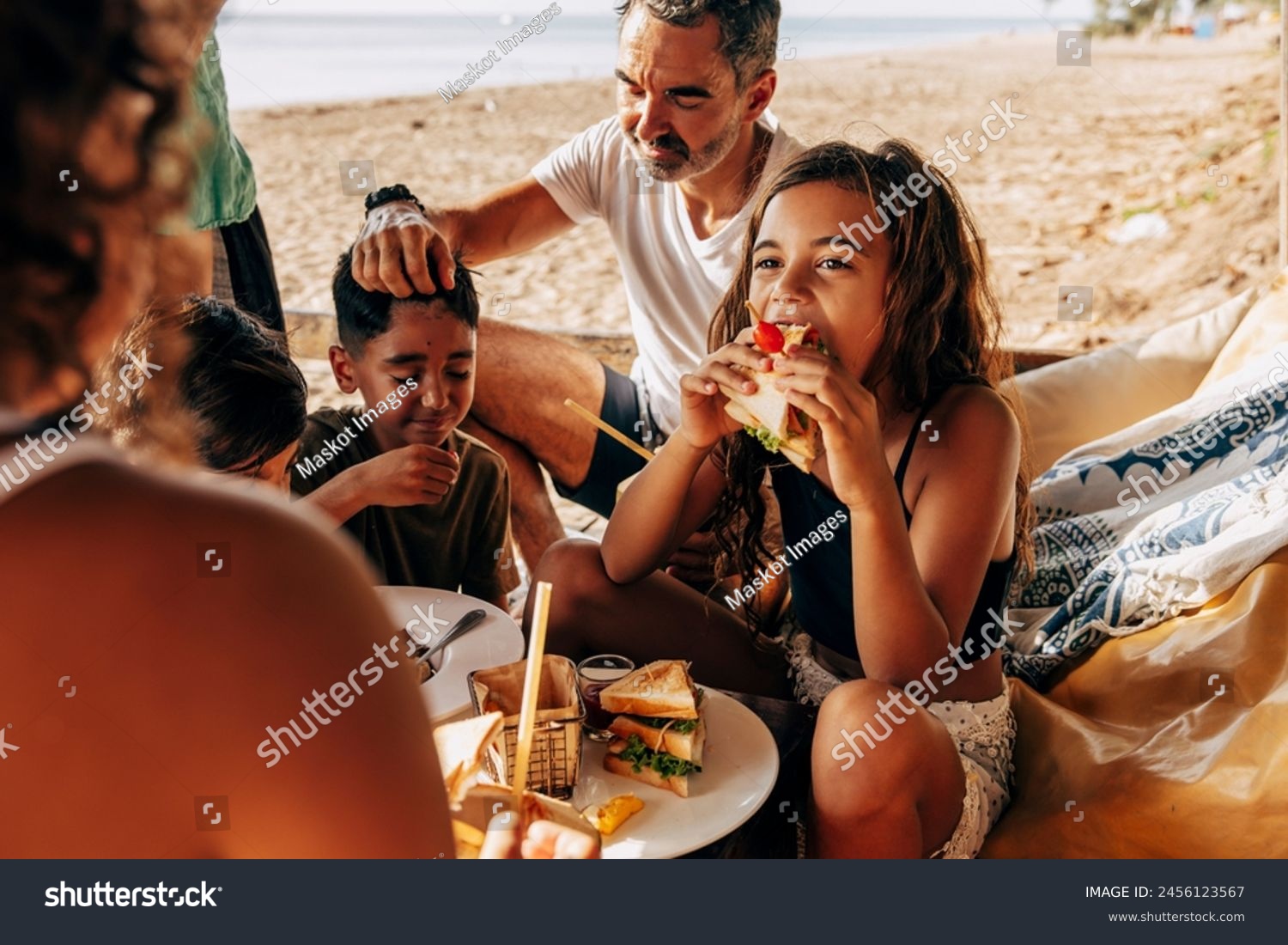Girl eating sandwich sitting with family in beach hut on vacation