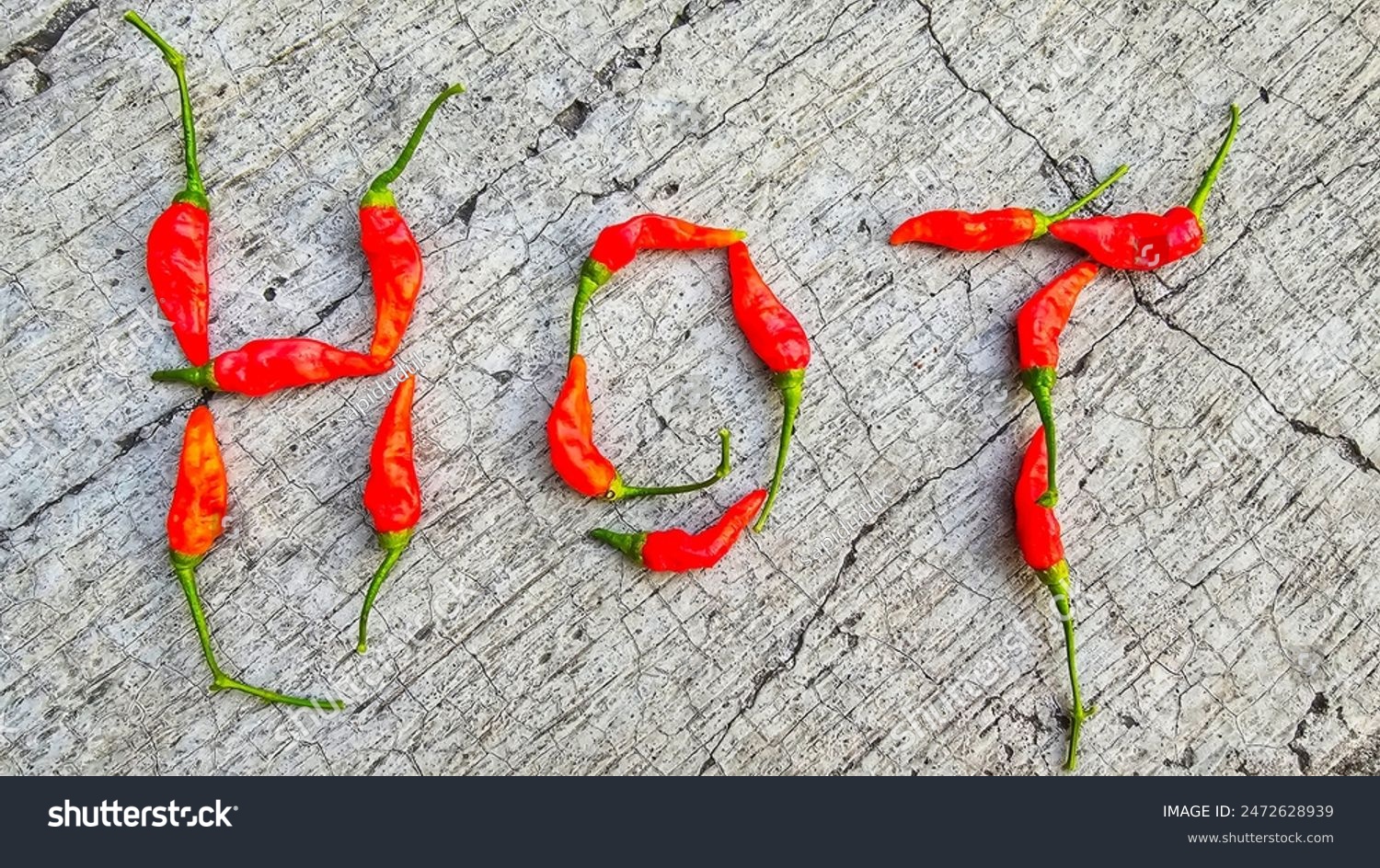 Red chili peppers arranged to spell the word "HOT" on a textured concrete surface, symbolizing spiciness and heat. This creative food arrangement highlights the vibrant colors and natural shape of the