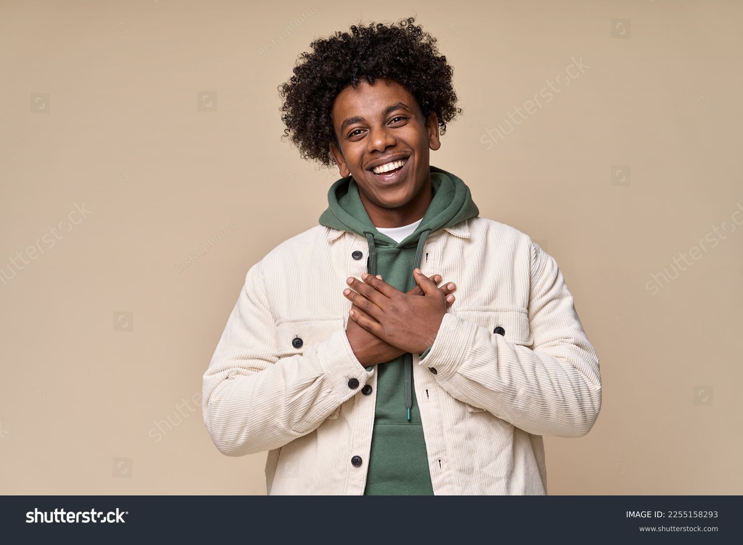 Happy pleased excited grateful African American teen guy holding hands on chest expressing gratitude, feeling trust hope love in heart, impressed with kindness isolated on beige background. 库存照片