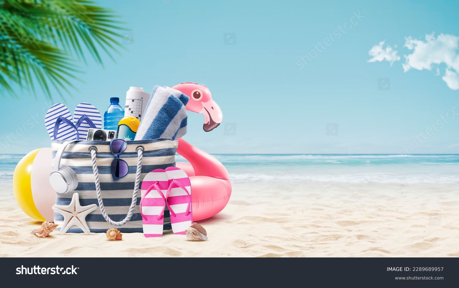 Beach bag with accessories and cute inflatable flamingo on a tropical beach, summer vacations and travel concept Stock Photo