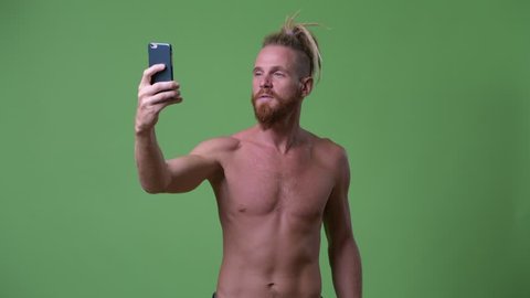 Happy handsome muscular bearded man with dreadlocks taking selfie while flexing arm shirtless Stockvideo
