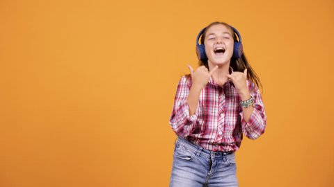 Happy young girl jumping while listening music in headphones isolated over an orange yellow background in studio Stock Video