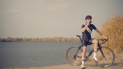 Bike Cyclist In Helmet Relaxing After Workout And Drinking Water. Cyclist In Helmet Relaxing After Workout And Drinking Water. Cardio Athlete Man Drinking Isotonic Before Cycling. Triathlete Restingの動画素材