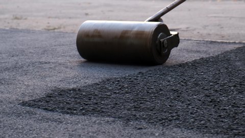 The worker pushes a manual roller for asphalt paving of the sidewalk.. Road works close-up Video stock