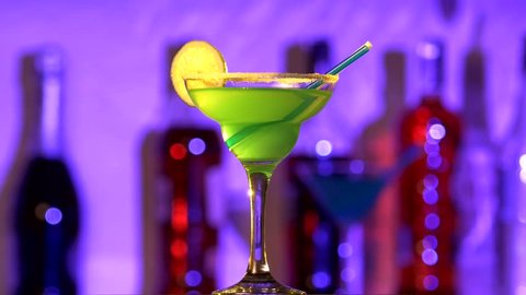 Green and yellow cocktail with lemon decortion, tubules and coconut on edge, rotation, on blue background: stockvideo